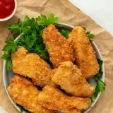 Crujientes tiras de pollo empanizadas con panko, servidas con perejil y salsas. El panko es un pan rallado japonés que da una textura extra crujiente.