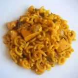 Fideuà de pollo con fideos rizados y trozos de pollo en salsa dorada, servida en plato blanco.