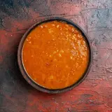 Un tazón de salsa emmy que lleva, con trozos de tomate y especias, sobre una superficie rústica.