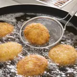 Croquetas doradas friéndose en aceite burbujeante, listas para ser disfrutadas. La bechamel para croquetas se transforma en esta delicia crujiente.
