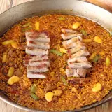 Paella de secreto con trozos de cerdo a la parrilla, judías verdes y trozos de naranja.