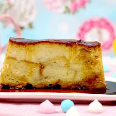 Un trozo de pan de calatrava con caramelo líquido sobre un plato blanco, adornado con merengues de colores y un limón al fondo.