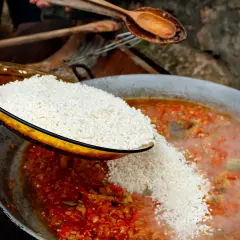 Se añade arroz a una paella de carne burbujeante con verduras rojas y verdes.