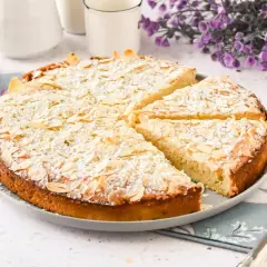Tarta de almendras dorada, espolvoreada con azúcar glas y almendras laminadas, lista para servir.