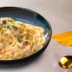 Deliciosa pasta con salmón cremoso, espolvoreada con perejil y queso rallado. Un plato perfecto para disfrutar.