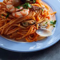 Espaguetis a la marinera con gambas, mejillones y almejas en una salsa roja, servidos en un plato azul.