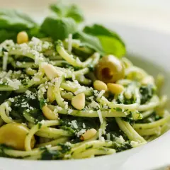 Deliciosa pasta al pesto, con piñones, aceitunas verdes y queso rallado, decorada con hojas de albahaca fresca.