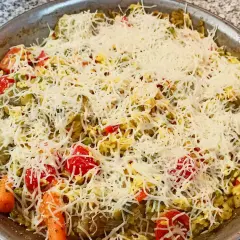 Arroz a la milanesa listo para hornear, cubierto con queso rallado y vegetales frescos como tomates, zanahorias y guisantes.
