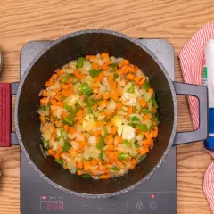 Verduras picadas (zanahoria, pimiento, cebolla) sofriéndose en una olla, listas para añadir lentejas con arroz.