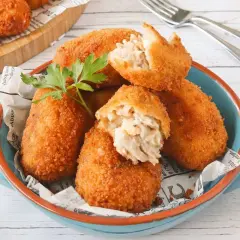 Croquetas de atún doradas y crujientes, servidas en un cuenco azul. Una está partida, mostrando su cremoso interior.
