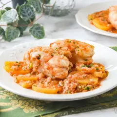 Delicioso rape con patatas en salsa de tomate y ajo, servido en un plato blanco con un tenedor y pan.
