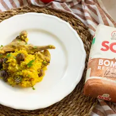 Plato de arroz con caracoles y trozos de carne, decorado con perejil. Al lado, un paquete de arroz SOS Bomba.