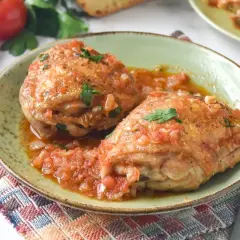 Dos jugosos contramuslos de pollo en salsa de tomate y cebolla, adornados con perejil fresco. Un plato casero y reconfortante.