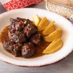 Sabrosa carne de cabra guisada con trozos de pimiento rojo y verde, servida con patatas gajo doradas.