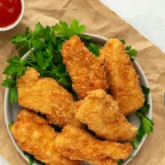 Crujientes tiras de pollo empanizadas con panko, servidas con perejil y salsas. El panko es un pan rallado japonés que da una textura extra crujiente.