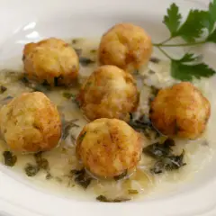Seis albóndigas de merluza doradas flotan en una cremosa salsa verde con perejil fresco.