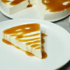 Una porción de tarta de cuajada, cremosa y blanca, bañada en un sirope dorado. El postre perfecto para un momento dulce.