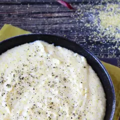 Cremosa polenta que es, servida en sartén negra, espolvoreada con pimienta negra.
