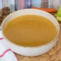 Un tazón de caldo de carne humeante, con un trozo de carne y verduras frescas al lado.
