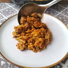 Un cucharón sirve arroz con secreto, un plato sabroso con carne y verduras, en un plato blanco.