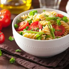 Un delicioso plato de pasta con verduras frescas, como tomates cherry, guisantes y perejil, servido en un cuenco blanco.