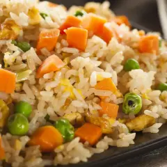 Arroz tres delicias con guisantes verdes, trozos de zanahoria y huevo revuelto, servido en un plato negro.