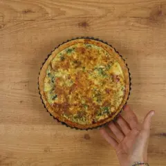 Un delicioso quiche de espinacas recién horneado, con una mano que lo sujeta suavemente.