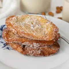 Tres torrijas de horchata, doradas y espolvoreadas con azúcar, apiladas en un plato con diseño floral azul.