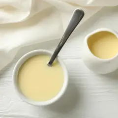 Leche evaporada en un tazón con cuchara y jarra, lista para usar en recetas.