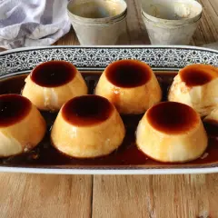 Seis deliciosos flanes de leche condensada, bañados en caramelo líquido, servidos en una bandeja decorada.