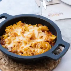 Macarrones al horno gratinados con queso fundido, servidos en una cazuela negra sobre un mantel de mármol.