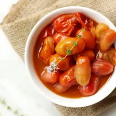 Un tazón blanco lleno de tomates cherry confitados, con una ramita de tomillo y una flor morada.