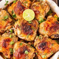 Muslos de pollo dorados y jugosos, horneados con limón y hierbas frescas, listos para servir.