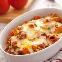 Macarrones con chorizo gratinados, cubiertos de queso derretido y perejil fresco, servidos en una fuente blanca.