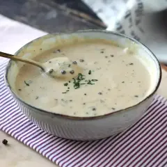 Un cuenco de cremosa salsa a la pimienta, con un toque de perejil picado y granos de pimienta negra esparcidos.