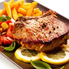 Chuletas de cerdo al horno jugosas, acompañadas de papas fritas crujientes, ensalada fresca y rodajas de limón.
