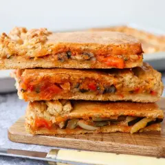 Tres porciones de empanada de verduras apiladas, mostrando el relleno de pimientos, calabacín y tomate.