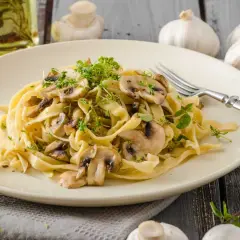 Deliciosa pasta con champiñones frescos y hierbas aromáticas, servida en un plato cremoso.