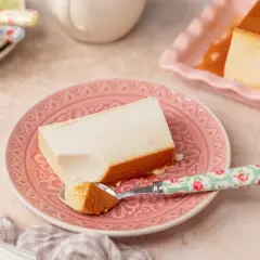 Un trozo de flan de queso cremoso con caramelo dorado, servido en un plato rosa.
