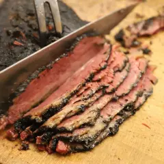 Un cuchillo corta un trozo de pastrami ahumado y jugoso, revelando su interior rosado.