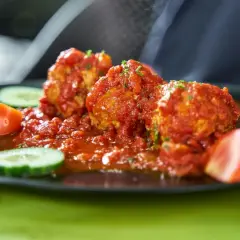 Albondigas con tomate, jugosas y cubiertas de salsa roja, acompañadas de rodajas de pepino y tomate fresco.