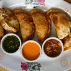 Empanadas de carne doradas y crujientes, servidas con tres salsas: chimichurri, picante y criolla.