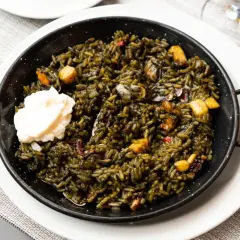 Arroz negro con sepia, un plato de mariscos oscuro y sabroso, servido en una paellera con una cucharada de alioli.
