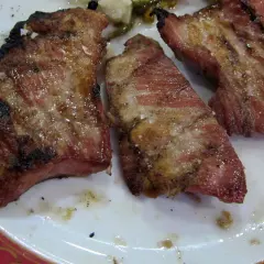 El secreto de cerdo a la parrilla, jugoso y con sal gruesa, servido en un plato blanco con borde rojo.