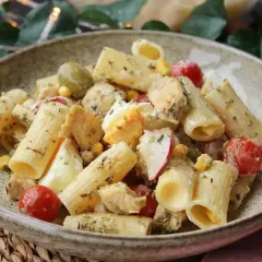 Deliciosa ensalada de pasta con pollo, huevo duro, tomates cherry, aceitunas y maíz, aderezada con hierbas.