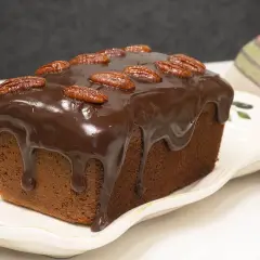 Bizcocho de plátano y chocolate cubierto de glaseado y nueces pecanas, listo para disfrutar.