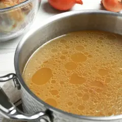 Olla con caldo de huesos burbujeante, junto a un bol con granos de pimienta y laurel, y otro con huesos.