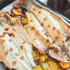 Lubina a la donostiarra recién horneada, con patatas y ajos dorados. Un plato delicioso y fácil de preparar.