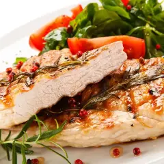 Jugoso solomillo de pavo a la parrilla, adornado con romero y pimienta rosa, acompañado de ensalada fresca y limón.