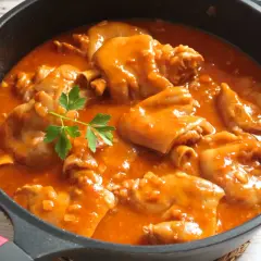 Manitas de cerdo en salsa roja, un plato tradicional español, servido en una sartén negra con perejil fresco.